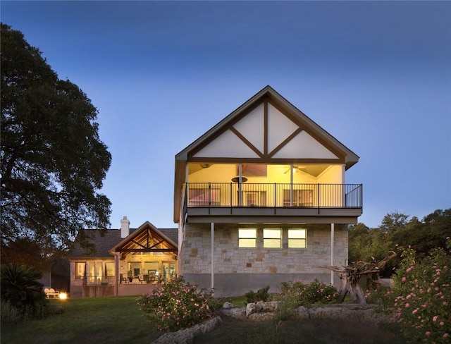 back house at dusk with a lawn and a balcony