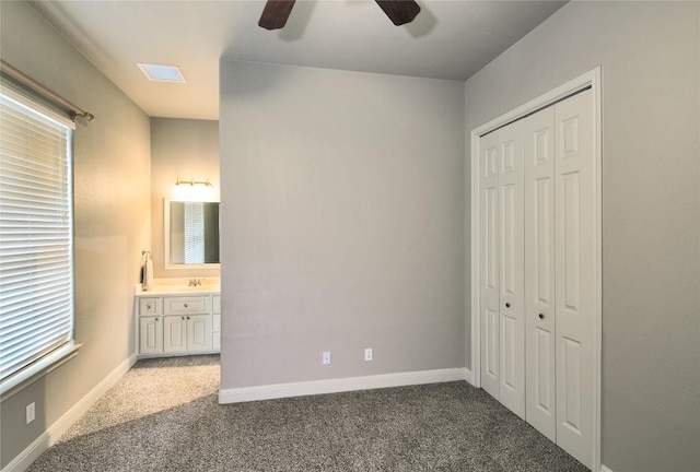 unfurnished bedroom featuring sink, ensuite bath, dark carpet, a closet, and ceiling fan