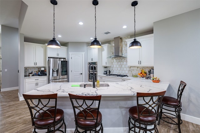 kitchen featuring white cabinetry, a kitchen breakfast bar, stainless steel appliances, decorative backsplash, and wall chimney range hood