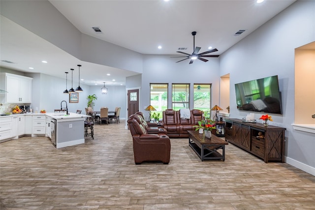 living room featuring sink, light hardwood / wood-style flooring, ceiling fan, and a high ceiling