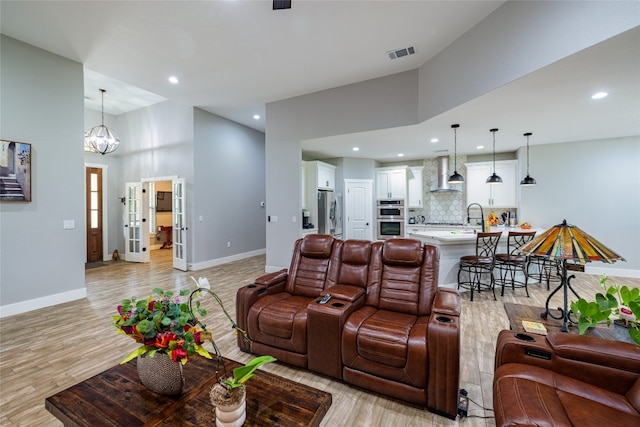 living room with high vaulted ceiling, an inviting chandelier, and light hardwood / wood-style floors