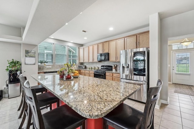 kitchen featuring light stone counters, black appliances, a spacious island, and a kitchen bar