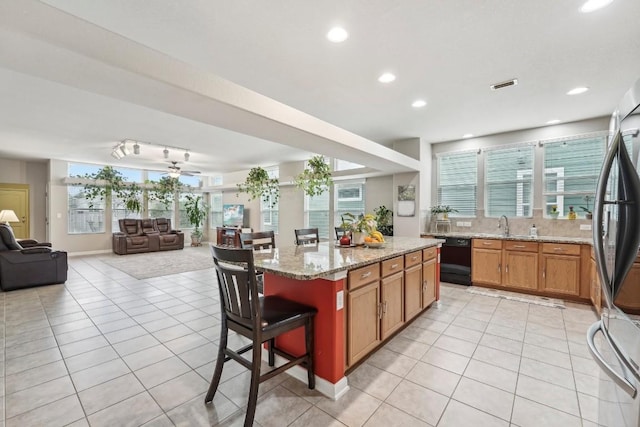 kitchen featuring light tile patterned floors, stainless steel fridge, dishwasher, a kitchen bar, and a kitchen island