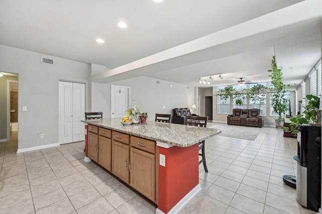 kitchen with a breakfast bar area, light tile patterned floors, a kitchen island, ceiling fan, and light stone countertops