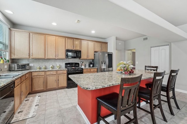 kitchen with a breakfast bar, a kitchen island, light stone countertops, decorative backsplash, and black appliances