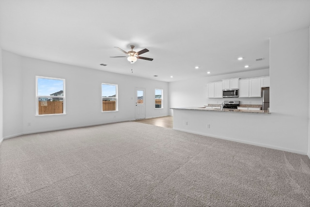 unfurnished living room featuring ceiling fan, light colored carpet, and sink