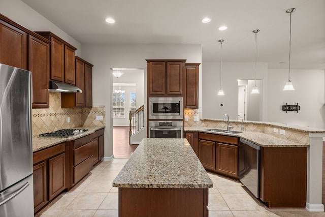 kitchen with appliances with stainless steel finishes, decorative light fixtures, sink, a center island, and light stone countertops