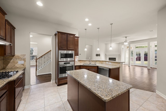 kitchen featuring backsplash, hanging light fixtures, a center island, stainless steel appliances, and light stone countertops