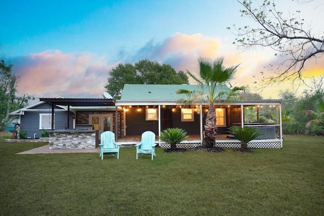 back house at dusk with french doors, a yard, a sunroom, and a patio