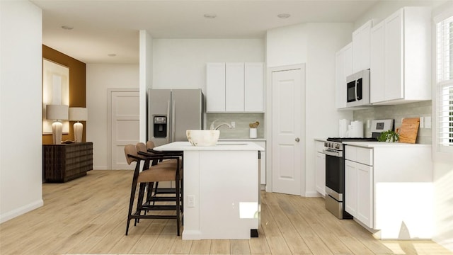 kitchen with appliances with stainless steel finishes, a kitchen breakfast bar, a center island with sink, and white cabinets