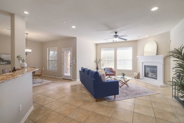 tiled living room with ceiling fan with notable chandelier and a textured ceiling