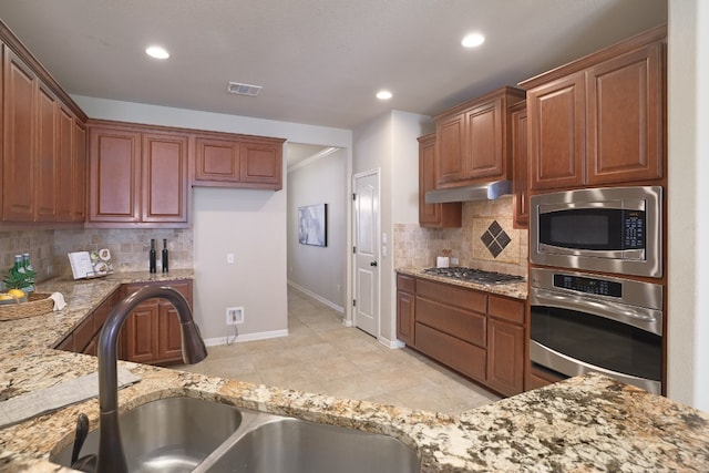 kitchen with light tile patterned flooring, appliances with stainless steel finishes, sink, decorative backsplash, and light stone countertops