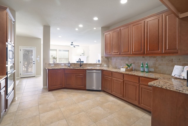 kitchen with sink, light stone counters, ceiling fan, stainless steel appliances, and decorative backsplash