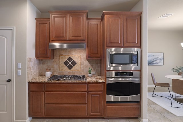 5025 Patagonia Pass, Austin, TX 78738 - kitchen featuring stainless steel appliances, tasteful backsplash, light stone counters, and brown cabinets