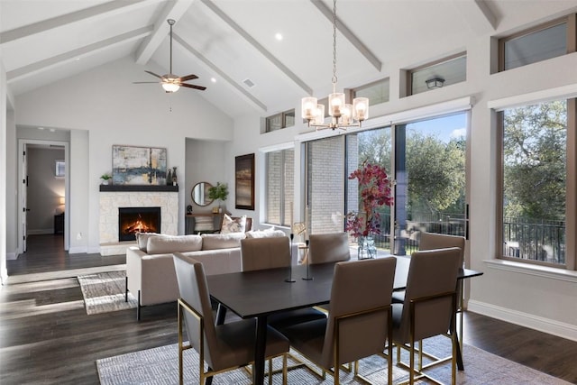 dining area with a stone fireplace, ceiling fan with notable chandelier, high vaulted ceiling, beamed ceiling, and dark hardwood / wood-style flooring