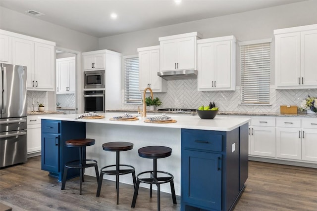 kitchen with a kitchen bar, a center island with sink, appliances with stainless steel finishes, dark hardwood / wood-style flooring, and white cabinets