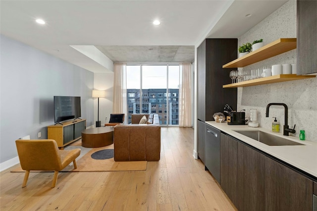 kitchen featuring dark brown cabinetry, sink, light wood-type flooring, dishwasher, and expansive windows