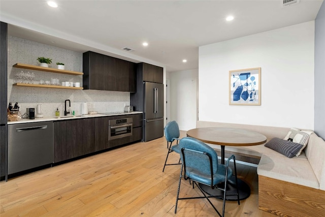 kitchen featuring sink, light hardwood / wood-style flooring, dark brown cabinets, stainless steel appliances, and decorative backsplash