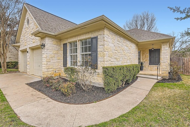 ranch-style house featuring a shingled roof, concrete driveway, fence, stone siding, and a front lawn