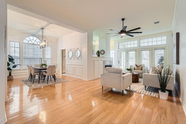 living area with a decorative wall, ceiling fan with notable chandelier, a fireplace, ornamental molding, and light wood finished floors