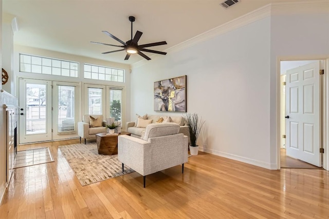 living area featuring ceiling fan, light wood-style flooring, visible vents, baseboards, and crown molding