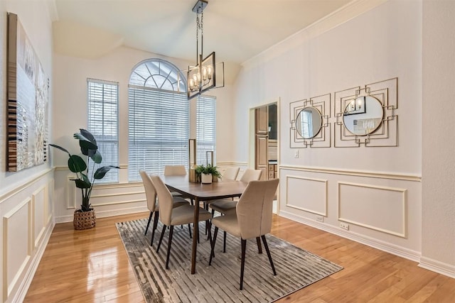 dining space featuring crown molding, a notable chandelier, a decorative wall, and light wood finished floors