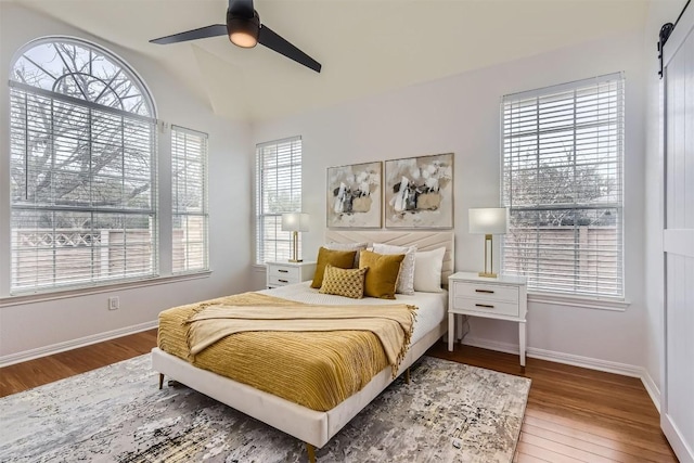 bedroom featuring a barn door, wood finished floors, a ceiling fan, and baseboards