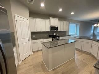 kitchen with light wood-type flooring, a center island, white cabinets, and appliances with stainless steel finishes