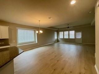 interior space featuring a raised ceiling, ceiling fan with notable chandelier, and light hardwood / wood-style flooring