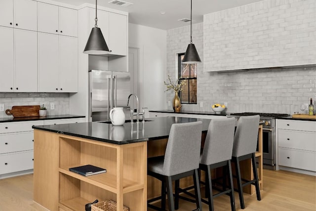 kitchen featuring high quality appliances, white cabinetry, a kitchen breakfast bar, hanging light fixtures, and a kitchen island with sink