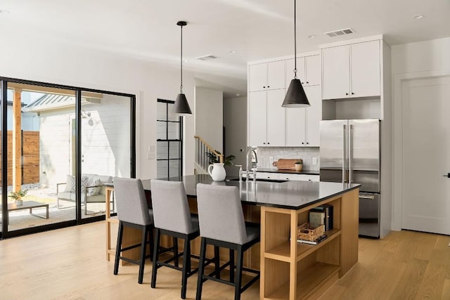 kitchen featuring pendant lighting, white cabinets, a center island with sink, decorative backsplash, and high end refrigerator