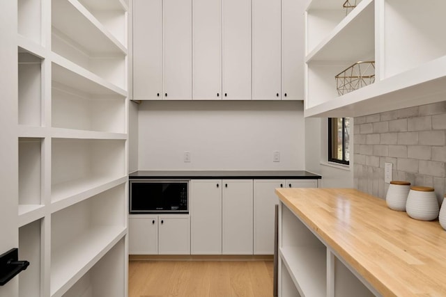 kitchen featuring black microwave, white cabinets, butcher block countertops, and light hardwood / wood-style floors