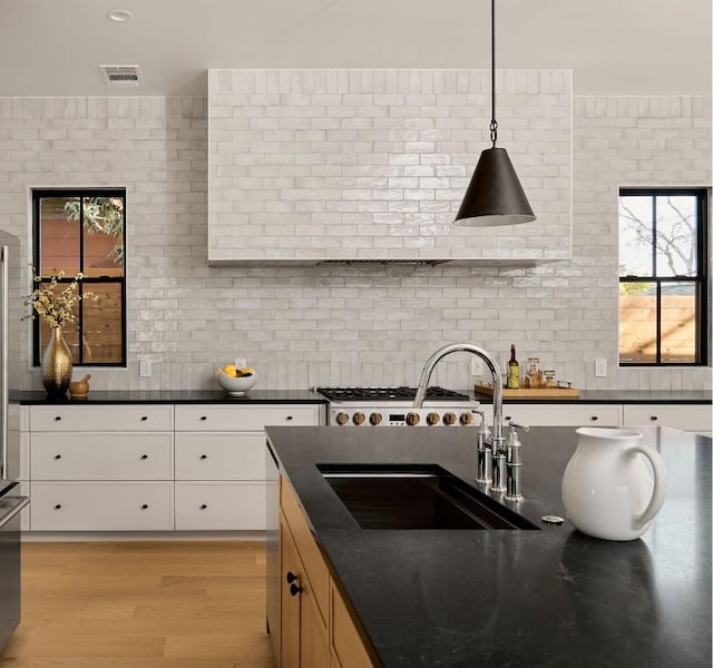 kitchen featuring pendant lighting, tasteful backsplash, sink, white cabinets, and light hardwood / wood-style flooring