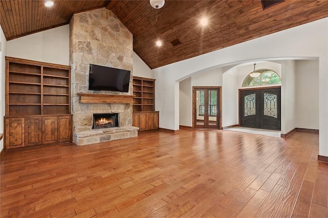 unfurnished living room with light wood-type flooring, french doors, wood ceiling, a stone fireplace, and high vaulted ceiling