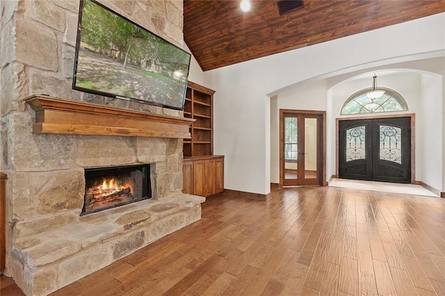 entrance foyer with french doors, high vaulted ceiling, wooden ceiling, a fireplace, and light hardwood / wood-style floors