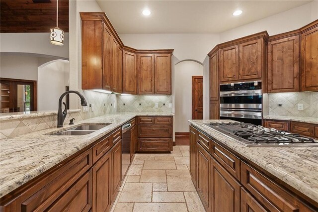 kitchen with sink, light stone counters, appliances with stainless steel finishes, pendant lighting, and backsplash