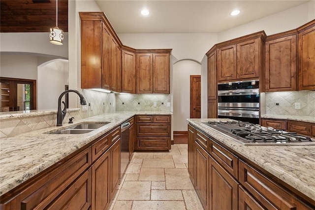 kitchen with decorative light fixtures, light stone countertops, sink, appliances with stainless steel finishes, and decorative backsplash