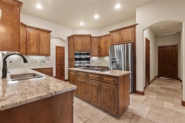 kitchen featuring sink, backsplash, stainless steel appliances, a center island, and light stone countertops