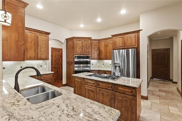 kitchen with sink, appliances with stainless steel finishes, a center island, light stone counters, and decorative light fixtures