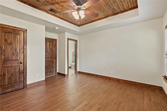 unfurnished bedroom featuring ensuite bath, wood ceiling, a raised ceiling, and wood-type flooring