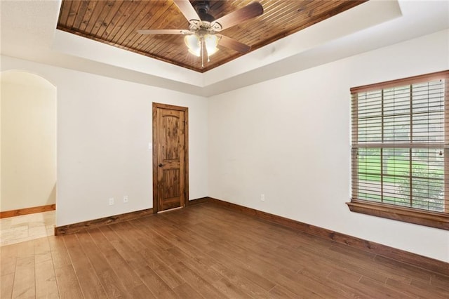 empty room with wood-type flooring, ceiling fan, a tray ceiling, and wood ceiling