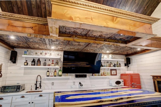 bar with white cabinetry, sink, and wood walls