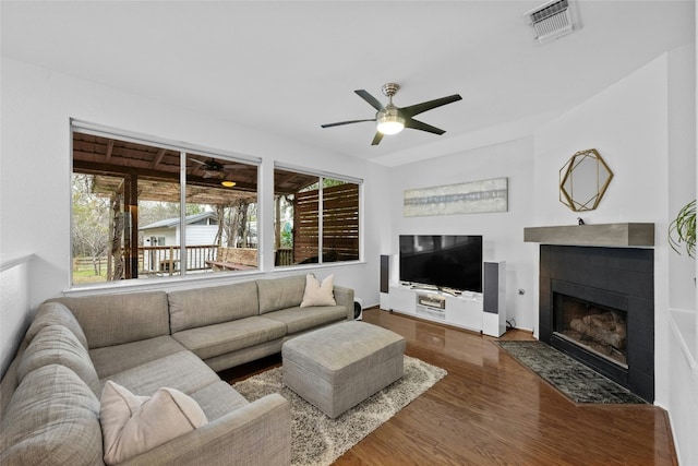 living room with ceiling fan, a tiled fireplace, and hardwood / wood-style floors