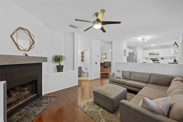 living room featuring ceiling fan, dark hardwood / wood-style flooring, and a tiled fireplace