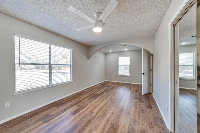 unfurnished room with ceiling fan, a healthy amount of sunlight, a textured ceiling, and light wood-type flooring