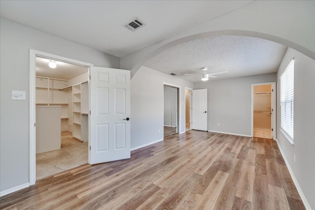 unfurnished bedroom featuring ensuite bath, a spacious closet, a textured ceiling, ceiling fan, and hardwood / wood-style floors