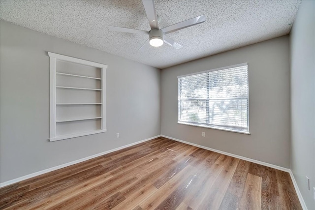 unfurnished room featuring ceiling fan, built in shelves, a textured ceiling, and hardwood / wood-style flooring