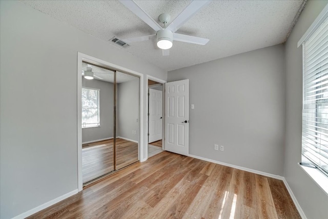 unfurnished bedroom featuring ceiling fan, a closet, light hardwood / wood-style flooring, and a textured ceiling