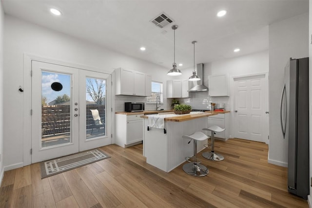 kitchen featuring appliances with stainless steel finishes, hanging light fixtures, a center island, white cabinets, and wall chimney exhaust hood