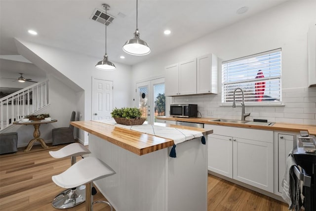 kitchen featuring wood counters, sink, a breakfast bar area, white cabinets, and hanging light fixtures